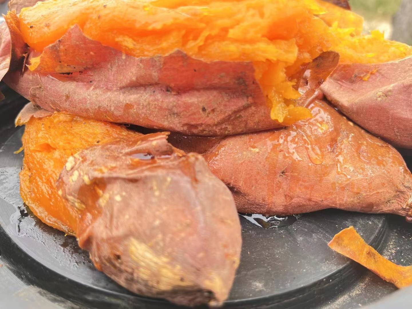一个刚出炉的烤烟薯放置在黑色陶瓷盘中,表皮微焦裂开,露出金黄色流油的内馅,热气袅袅升起,旁边放有一小块黄油,展现其香甜软糯的诱人质感 烤烟薯特写