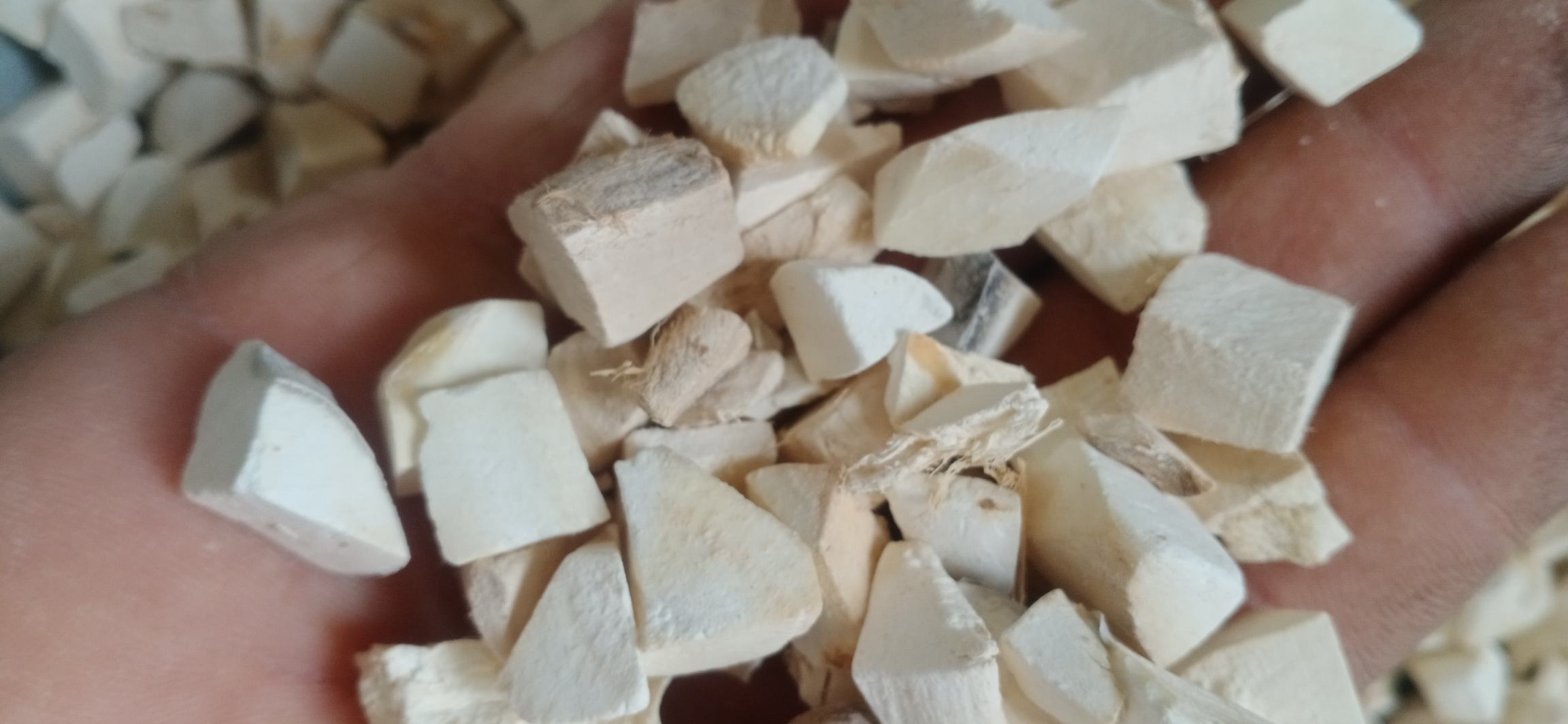 一名工人正在手工切割中草药粉葛根,案板上摆放着新鲜切开的粉葛片,断面洁白湿润,背景为传统中药加工厂环境,可见晾晒架和药材筐 中草药粉葛的切片加工过程