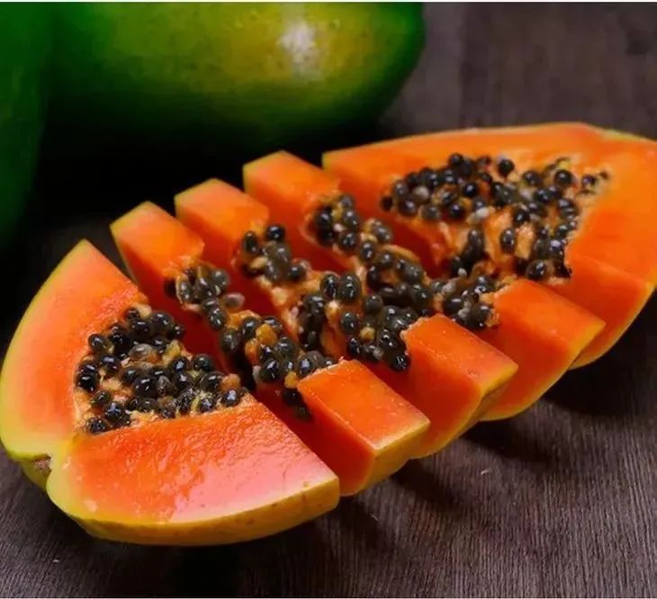 一颗成熟的红心木瓜被横向切开,露出鲜艳的橙红色果肉,果核呈黑色排列在中央,果肉饱满多汁,背景为浅色木质桌面,自然光线照射,突出其新鲜度和色泽 红心木瓜切开特写