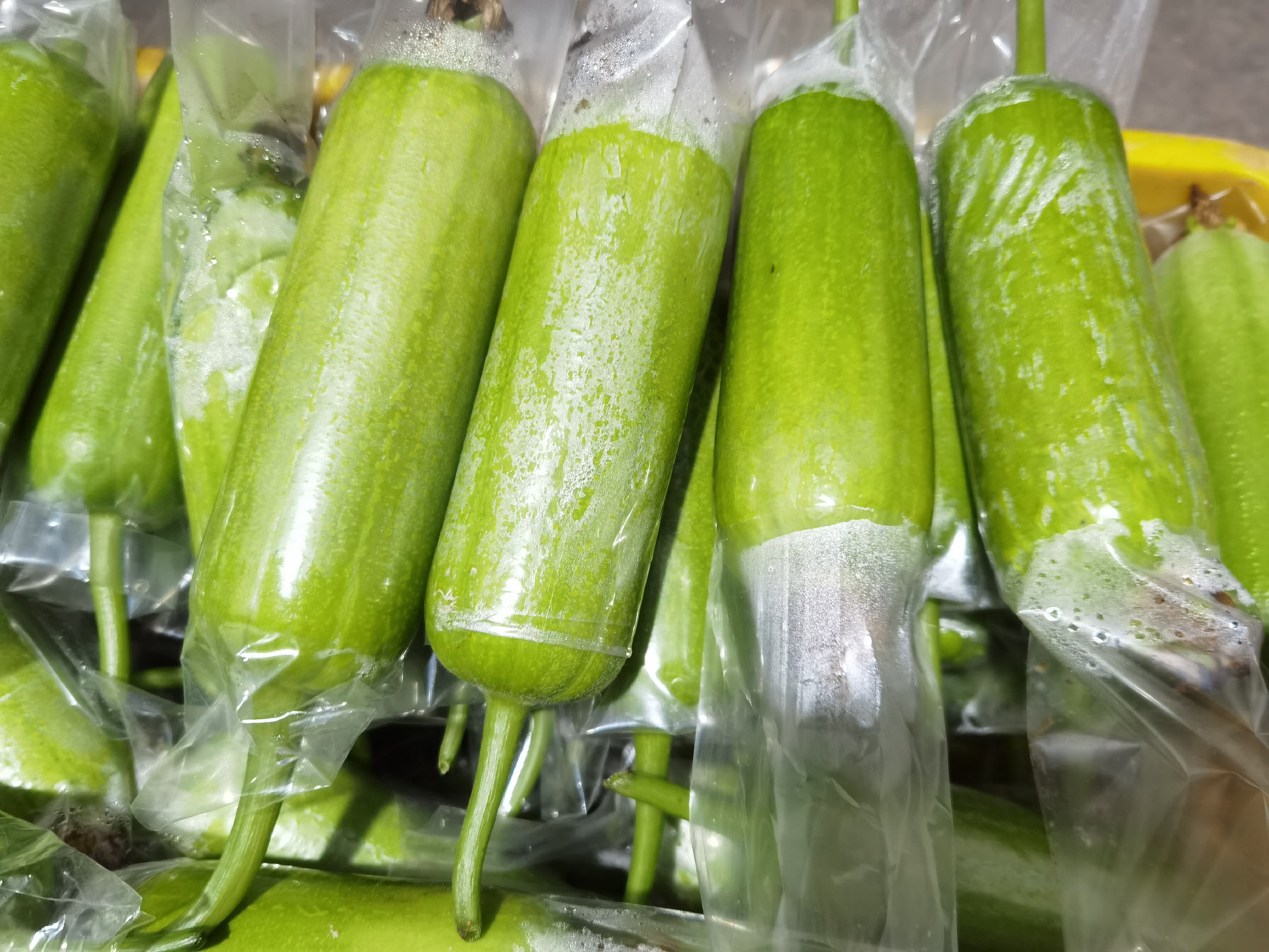 一位消费者在农贸市场摊位前仔细挑选玉菇甜瓜,摊位摆放整齐,背景有其他农产品 市场中正在挑选玉菇甜瓜的消费者