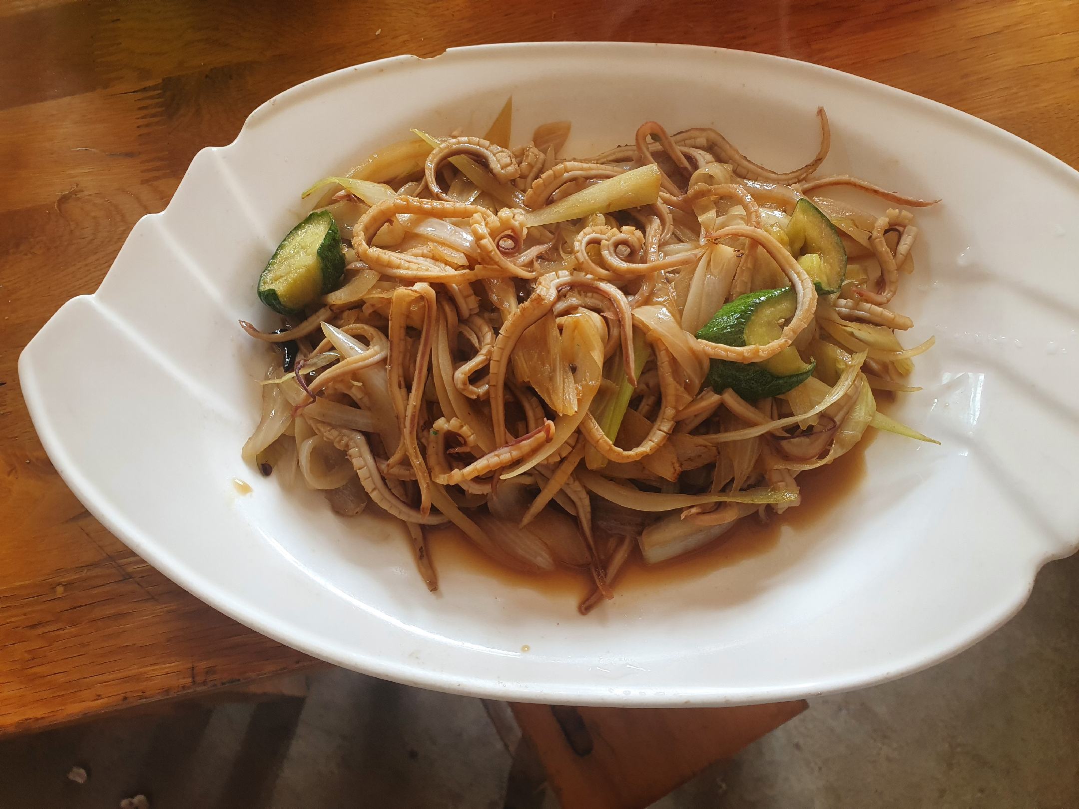 一盘色彩鲜艳的凉拌小鱿鱼特写，配有黄瓜丝、香菜和红油光泽，盛于青花瓷盘中