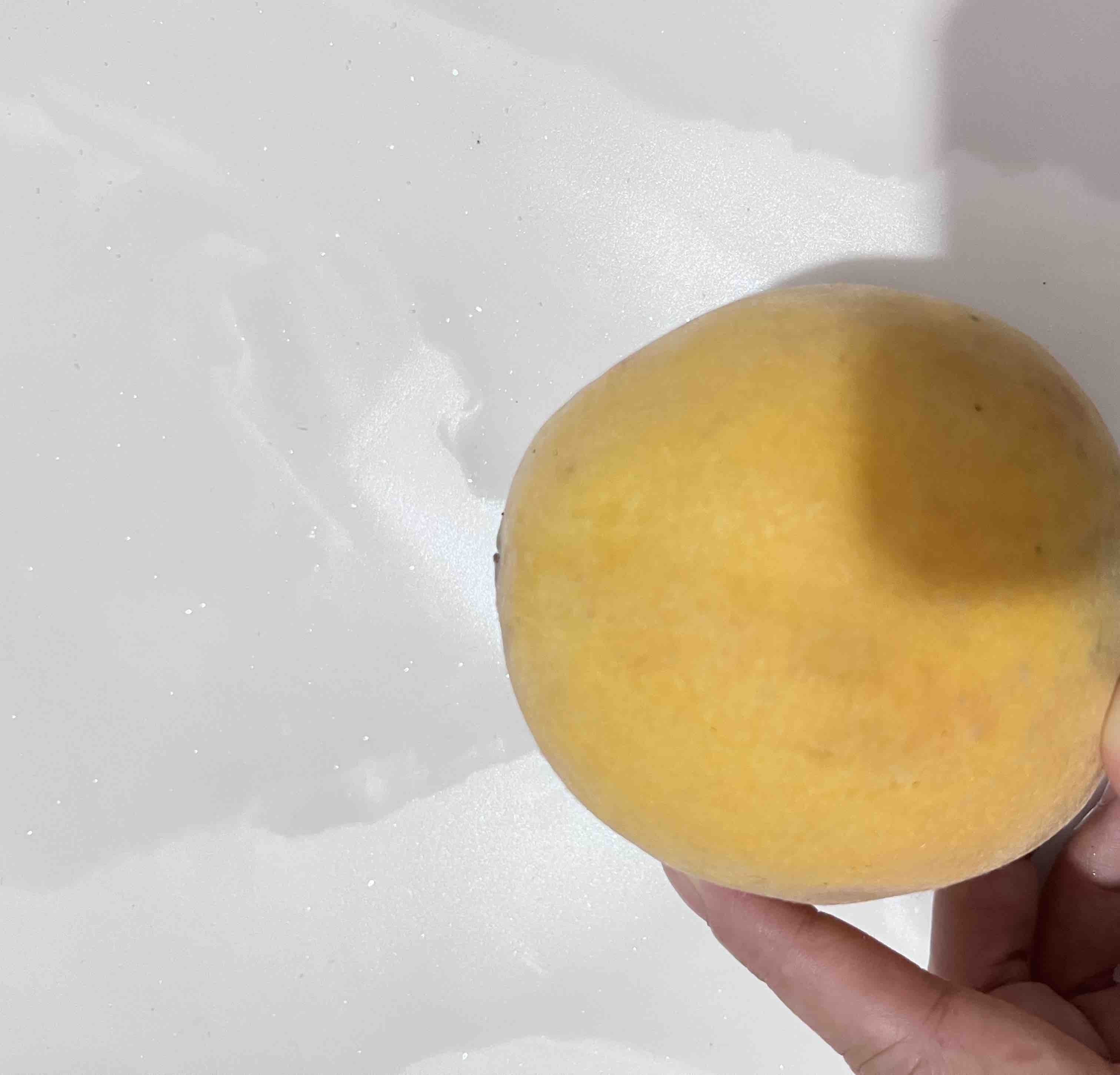 一位成年人的手正在用拇指轻压黄桃的果肩部位,动作轻柔,背景为市场摊位,周围摆放多个黄桃,突出‘手感测试’场景 手部正在轻压黄桃测试成熟度