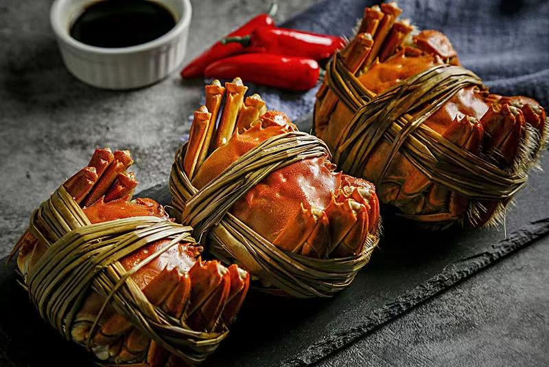 一只新鲜的大闸蟹摆放在传统中式餐桌上,旁边是米饭和家常菜 大闸蟹与传统餐桌