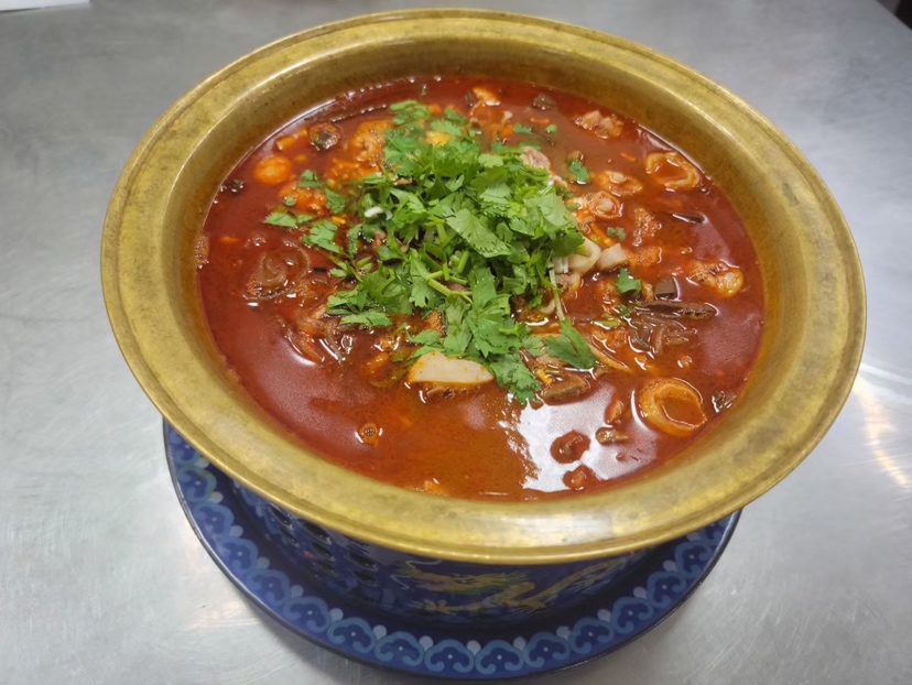 高端中餐厅内,厨师正在将新鲜禹州香菜点缀于一碗热腾腾的羊杂汤表面,香菜叶片舒展翠绿,与乳白色的汤体形成鲜明对比,蒸汽袅袅上升,展现食材的新鲜与香气释放过程 禹州香菜在餐饮应用中的摆盘展示