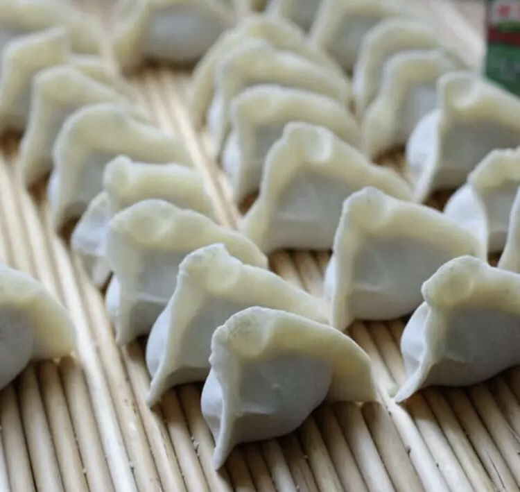 一位家庭主妇正在厨房中将切好的韭菜和萝卜混合搅拌成饺子馅 饺子制作过程