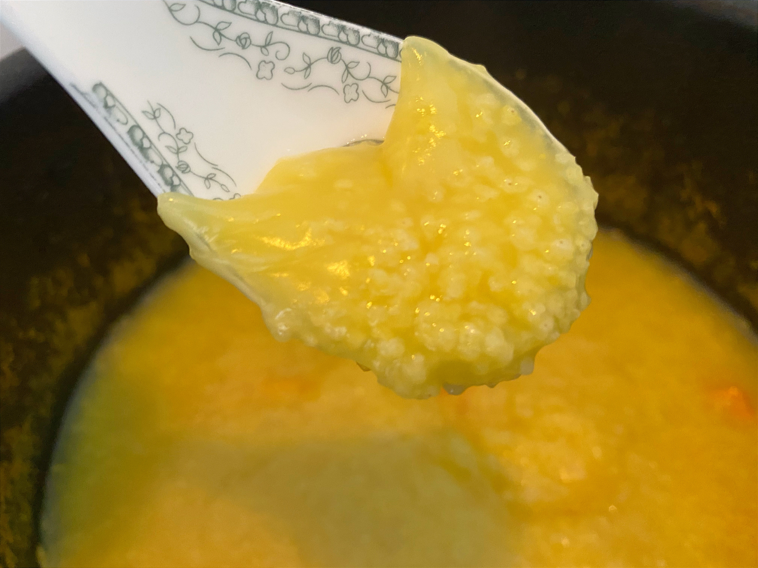 高清食物摄影:山西沁州黄小米粥盛于青瓷碗中,表面浮有金黄色米油,可见深褐色熟地黄软片与淡黄色党参片沉底,粥体浓稠挂勺,温度计显示62℃(最佳营养保留温度) 党参熟地黄小米粥成品特写