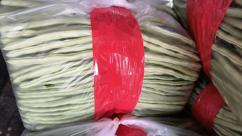 多款市售白扁豆包装整齐摆放在白色桌面上,包括透明塑料袋装、真空铝箔袋装及礼盒装,标签清晰可见生产日期、配料表和SC认证编号,旁边放置一支放大镜聚焦于‘生产日期’位置,强调信息可读性 白扁豆包装展示图