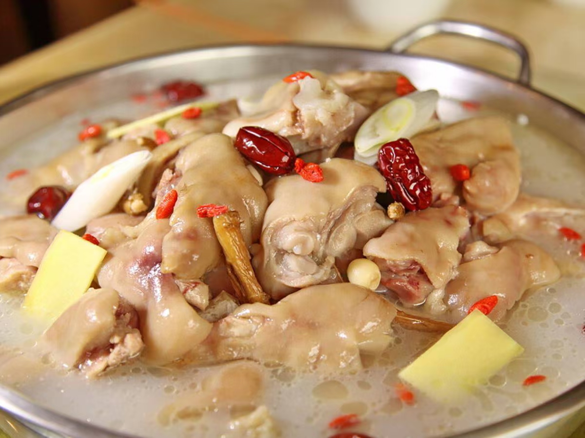 一口深色砂锅中盛满红棕色的猪蹄红枣汤,猪蹄色泽红亮,表皮油润有光泽,红枣沉浮其中,汤面微微泛油光,旁边摆放着木勺和青花瓷碗,背景为厨房操作台 猪蹄红枣炖汤全景