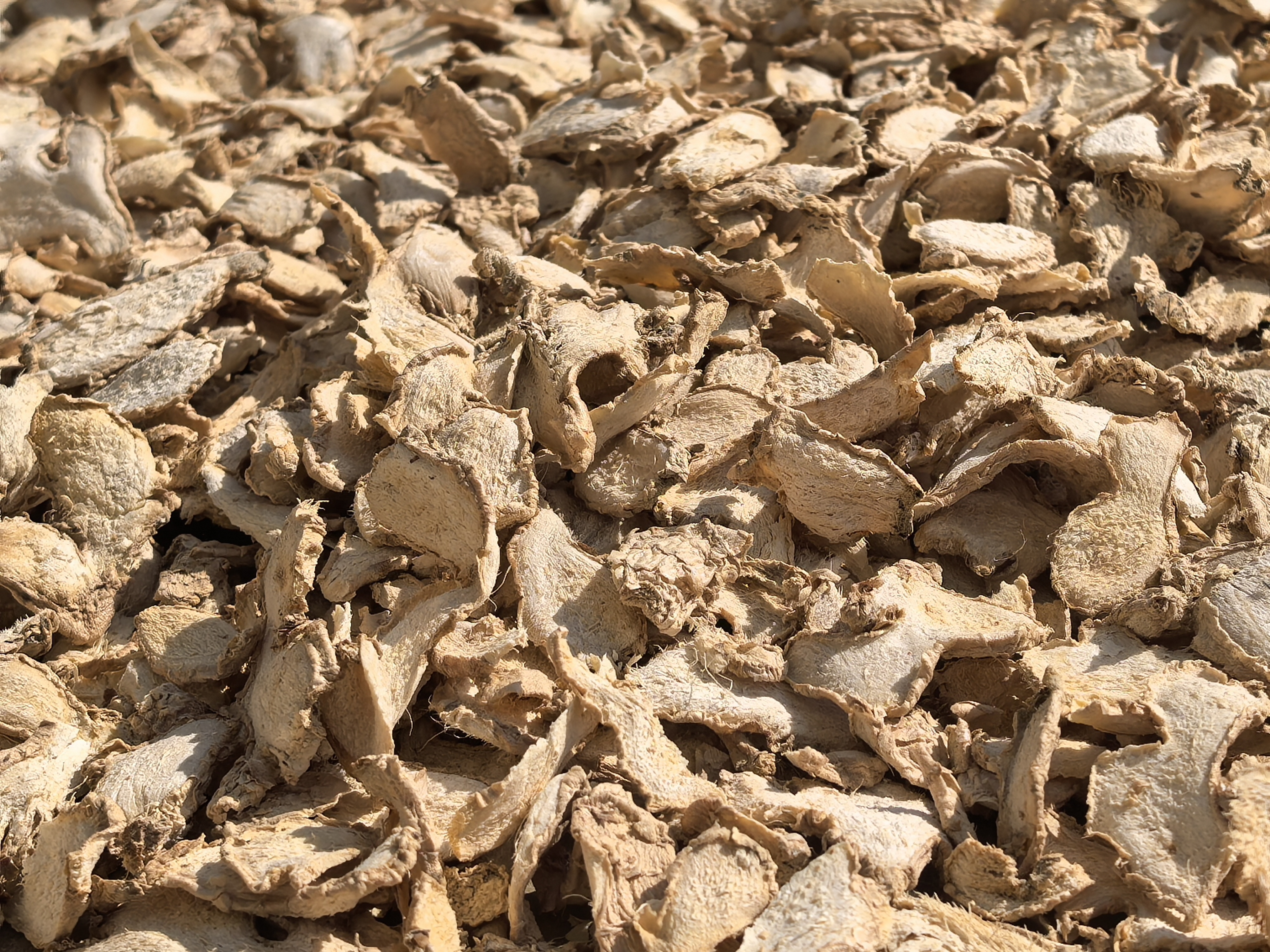 特写镜头展示数片风干姜,呈不规则薄片状,边缘卷曲,表面有明显纹理和皱褶,颜色为深琥珀色至棕黄色。光线侧照凸显质感,背景为浅灰色麻布材质,突出天然有机感 风干姜片特写照片