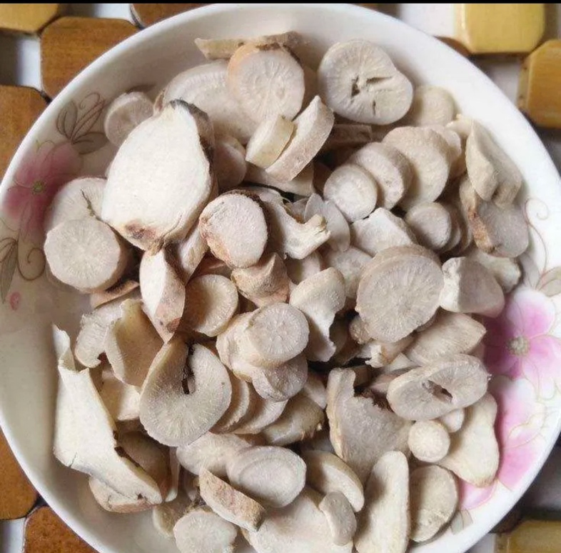 一位中年女性坐在中医诊所内,正在与身穿白大褂的女医生交谈,桌上摆放着脉枕、舌诊图和几味中药材,包括鹿鞭切片、枸杞、当归等,墙上挂着经络图 女性中医问诊场景