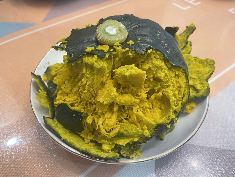一位家庭主妇正在厨房操作台上准备板栗南瓜,手中拿着菜刀,南瓜已被切成两半,金黄的瓜肉朝上,旁边有蒸锅和调料瓶,场景温馨,体现日常健康饮食氛围 家庭烹饪中的板栗南瓜