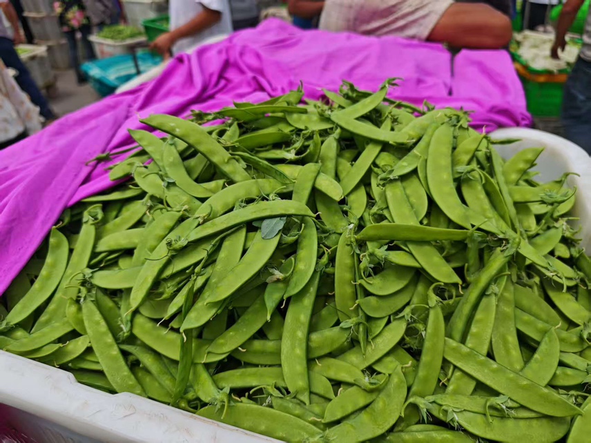 市场摊位上整齐摆放的新鲜荷兰豆,旁边有其他蔬菜供顾客挑选 荷兰豆在市场中被摆放在蔬菜摊位上出售