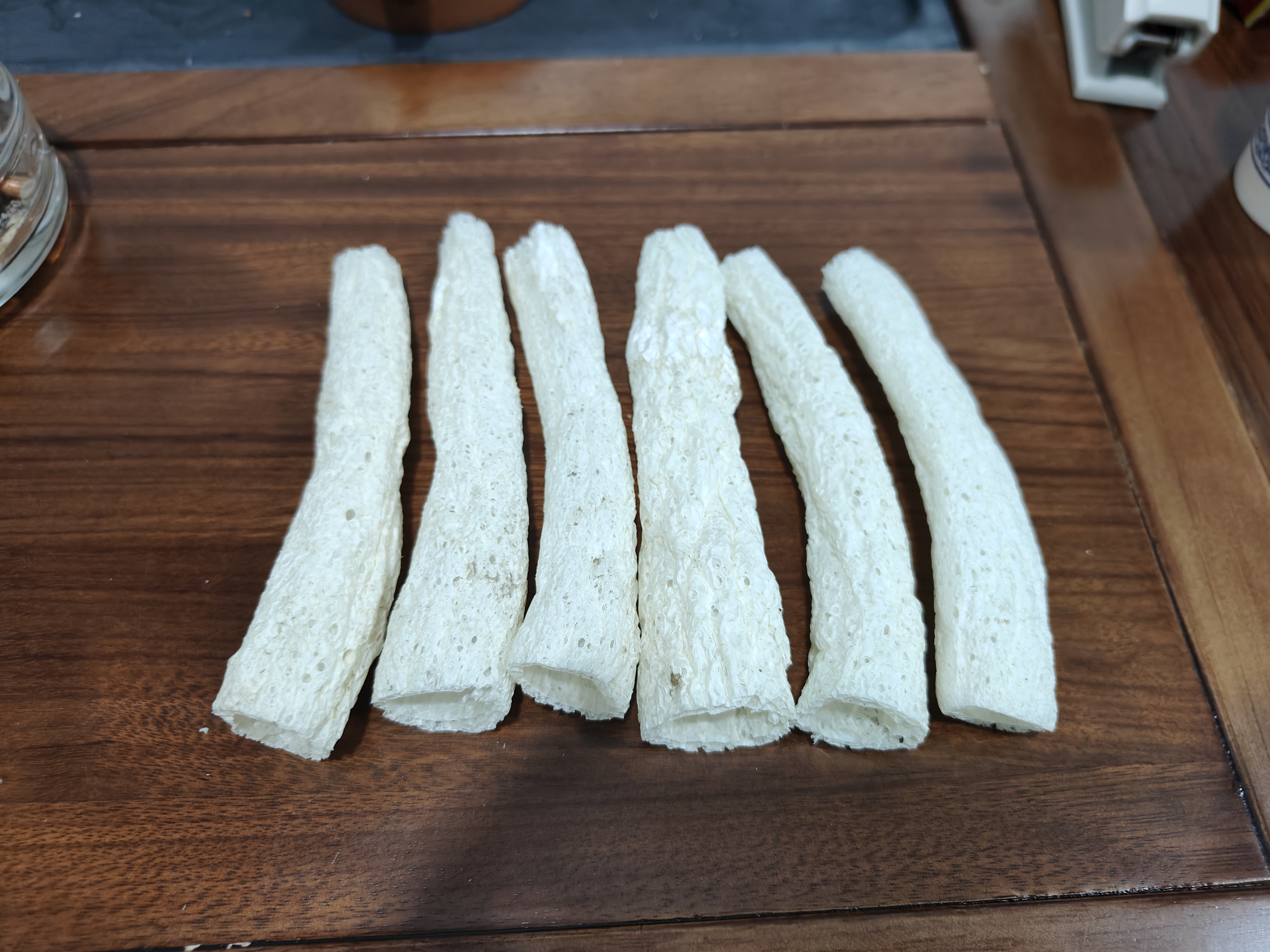 一碗透明玻璃盆中浸泡着数朵乳白色长裙竹荪,菌裙舒展如蕾丝裙摆,水中可见细小气泡附着在表面,旁边摆放着几片生姜和一瓶白醋,背景为厨房台面木质纹理 泡发中的长裙竹荪特写